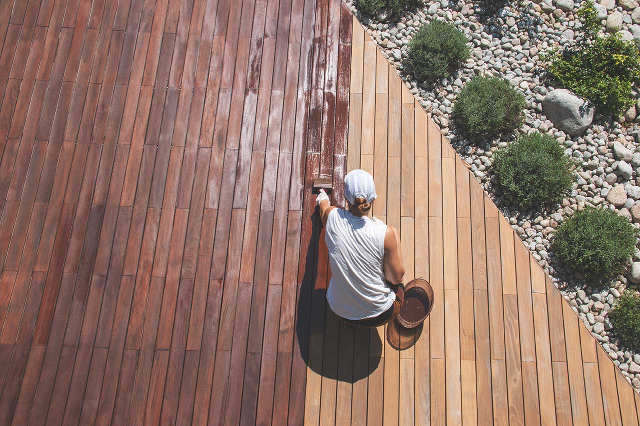 homeowner refinishing a wood deck in backyard